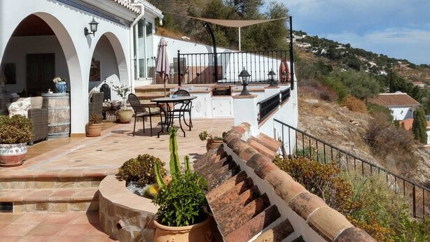 A white building with arches and a terrace with potted plants.