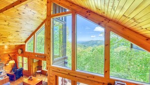 Una cabaña con ventanas amplias que ofrecen vistas de una cadena montañosa boscosa.