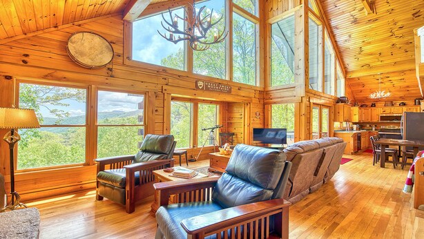 Una cabaña amplia con ventanas grandes, chimenea, comedor y televisor.