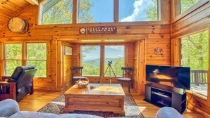 Una cabaña con paredes de madera, ventanas grandes, un televisor y un telescopio.
