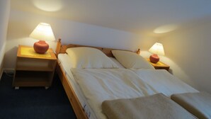 A neatly made bed with two bedside lamps, a wooden headboard, and a small wooden nightstand with a lamp. - South balcony with the sound of the sea, three-room apartment for 4-5 people. (Kellenhusen (Ostsee))
