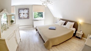 A bedroom with a large bed, a dresser, a window with a view of greenery, and a ceiling light fixture.