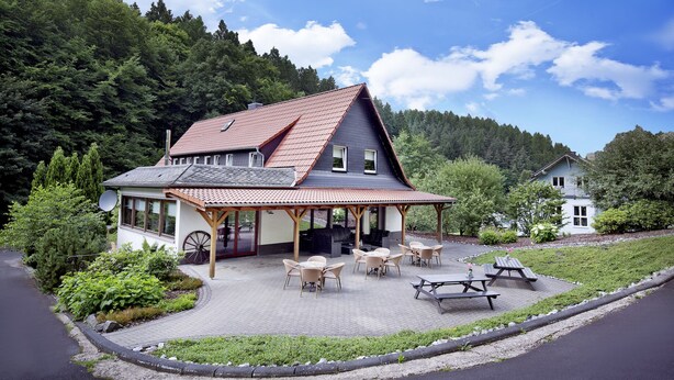 A house with a covered patio, outdoor seating, and a scenic forest backdrop.