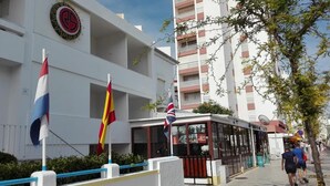 Ein Gebäude mit weißer Fassade, einer schwarz-weißen Flagge und einer Straßenbahnhaltestelle.