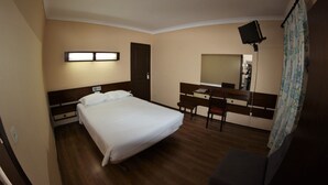 Ein Hotelzimmer mit Bett, Schreibtisch, Stuhl, Flachbildfernseher und Spiegel.