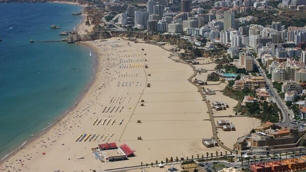 Luftaufnahme einer Küstenstadt mit einem langen Sandstrand, einer Marina und dichter Bebauung.