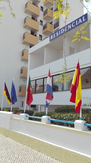 A building with a sign reading "RESIDENCIAL" and multiple flags in front. - Residencial Sol (Portimão)