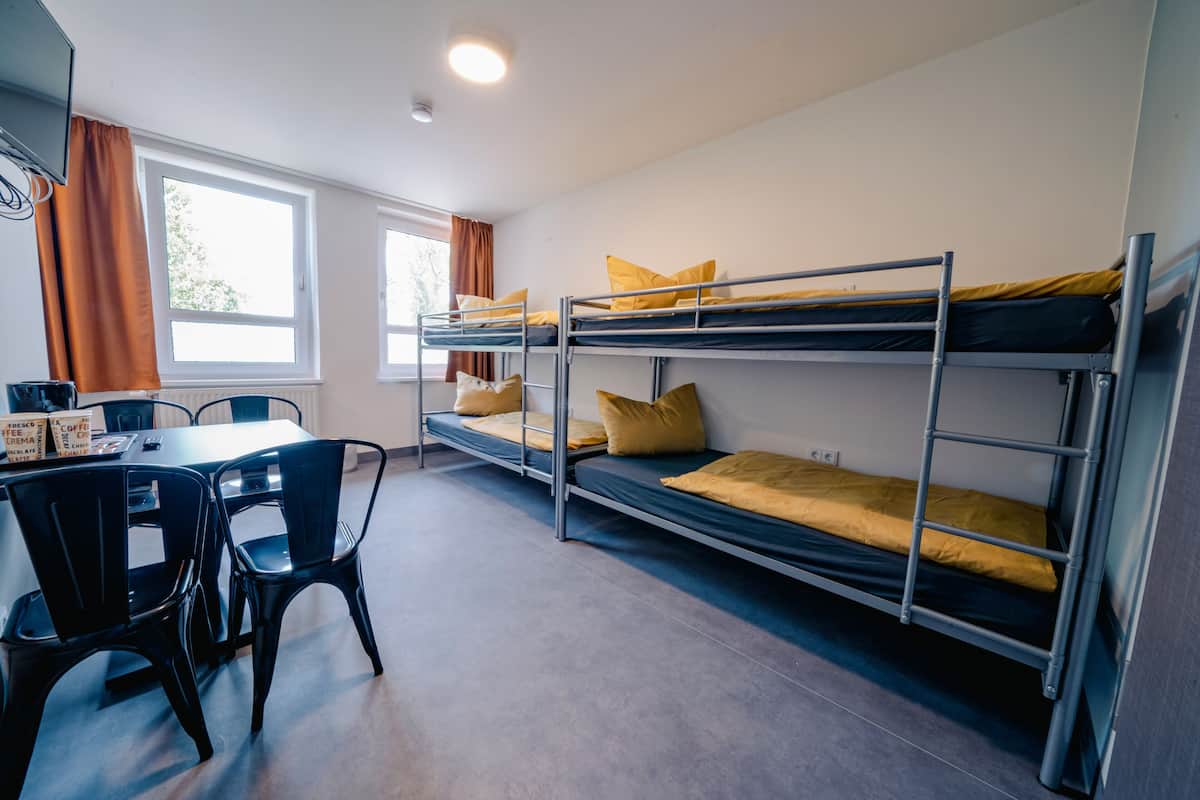 Ein Schlafsaalzimmer mit Etagenbetten, einem Tisch mit Stühlen und einem Fenster mit Vorhängen.