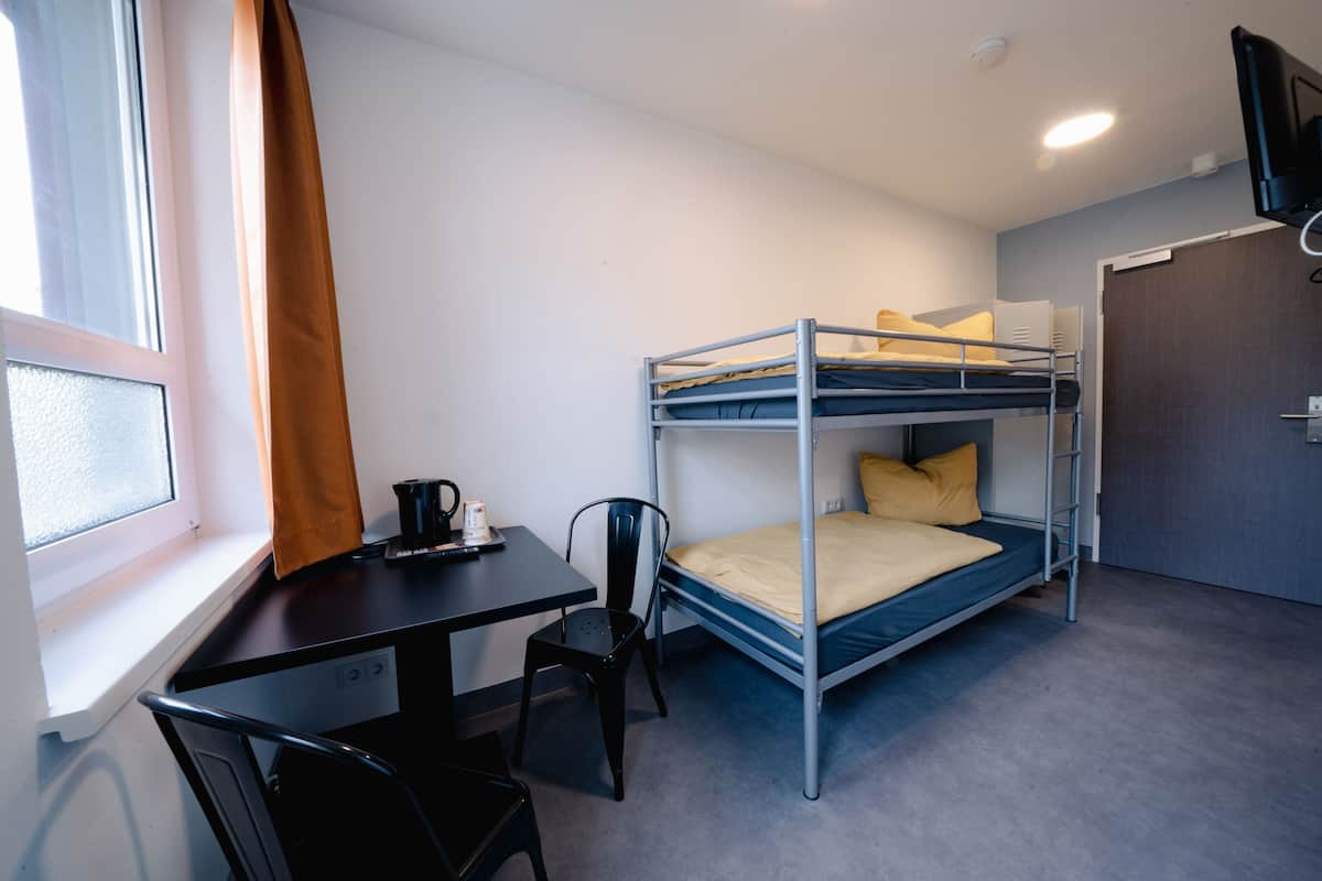 Ein Stockbett mit Schreibtisch und Stuhl, ein Fenster mit Vorhängen und eine Tür mit Fernseher darüber.