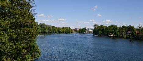 A river with trees on both sides, a bridge in the distance, and buildings along the riverbank.