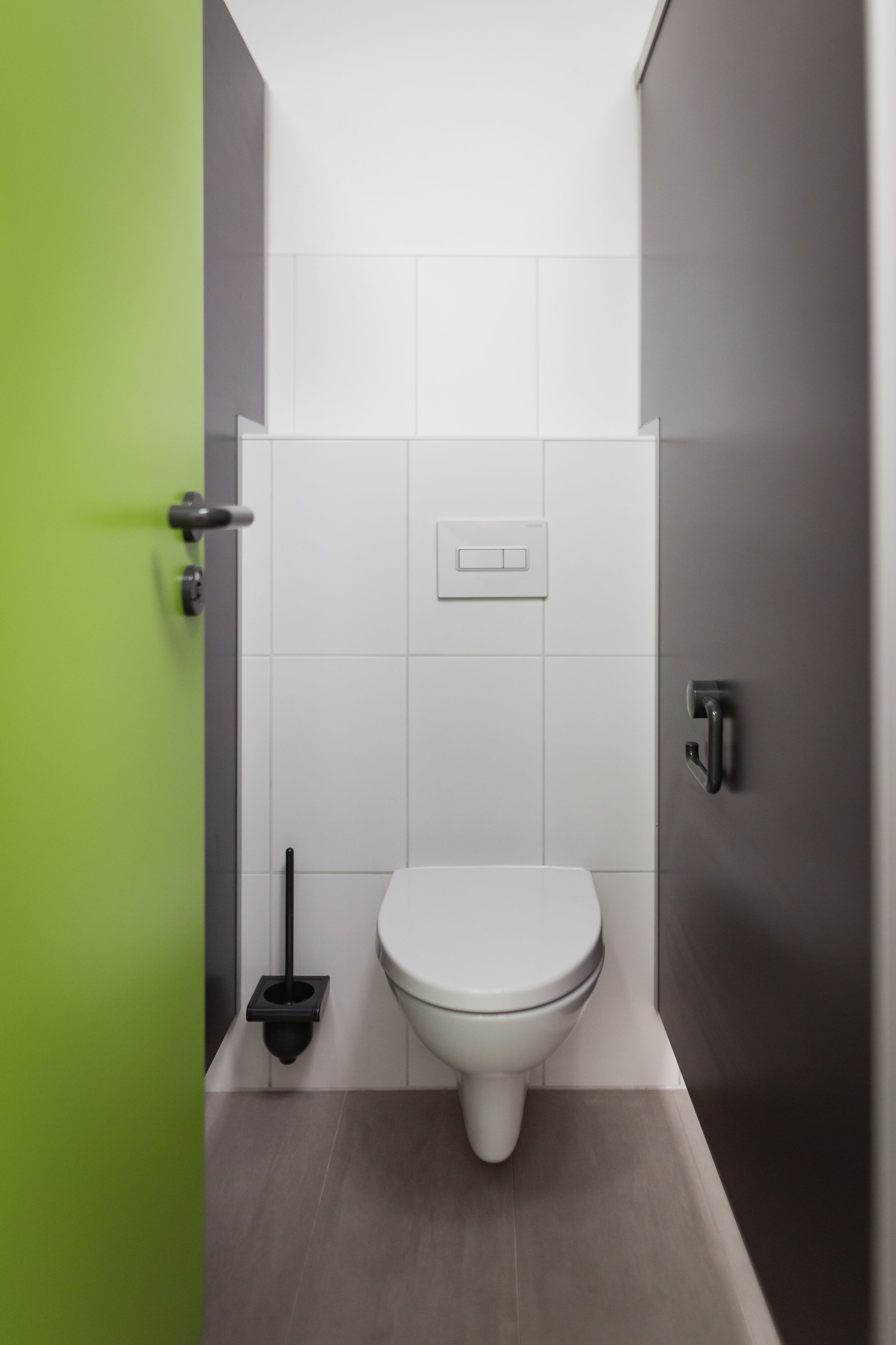 Un baño moderno con inodoro blanco, puerta verde y un escobillón negro.