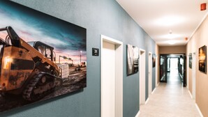 A hallway with a large painting of a construction vehicle, a door labeled "311", and a carpeted floor. - NEOHOSTEL Berlin (Berlin)