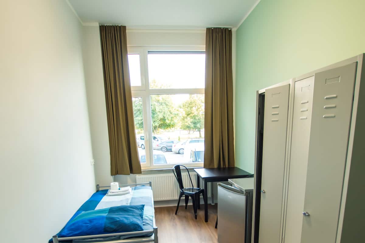 Ein Schlafsaalzimmer mit zwei Einzelbetten, einem Schreibtisch, einem Stuhl, einem Heizkörper und einem Fenster mit Vorhängen.