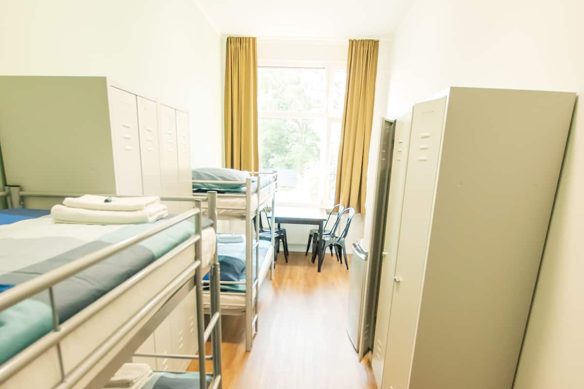 Ein Schlafsaalzimmer mit Etagenbetten, einem Schreibtisch, Stühlen und einem Fenster mit Vorhängen.