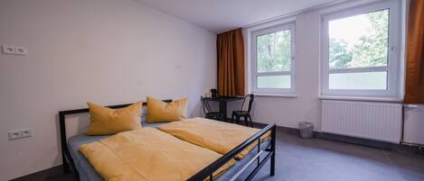 Un dormitorio con cama, escritorio y dos ventanas.