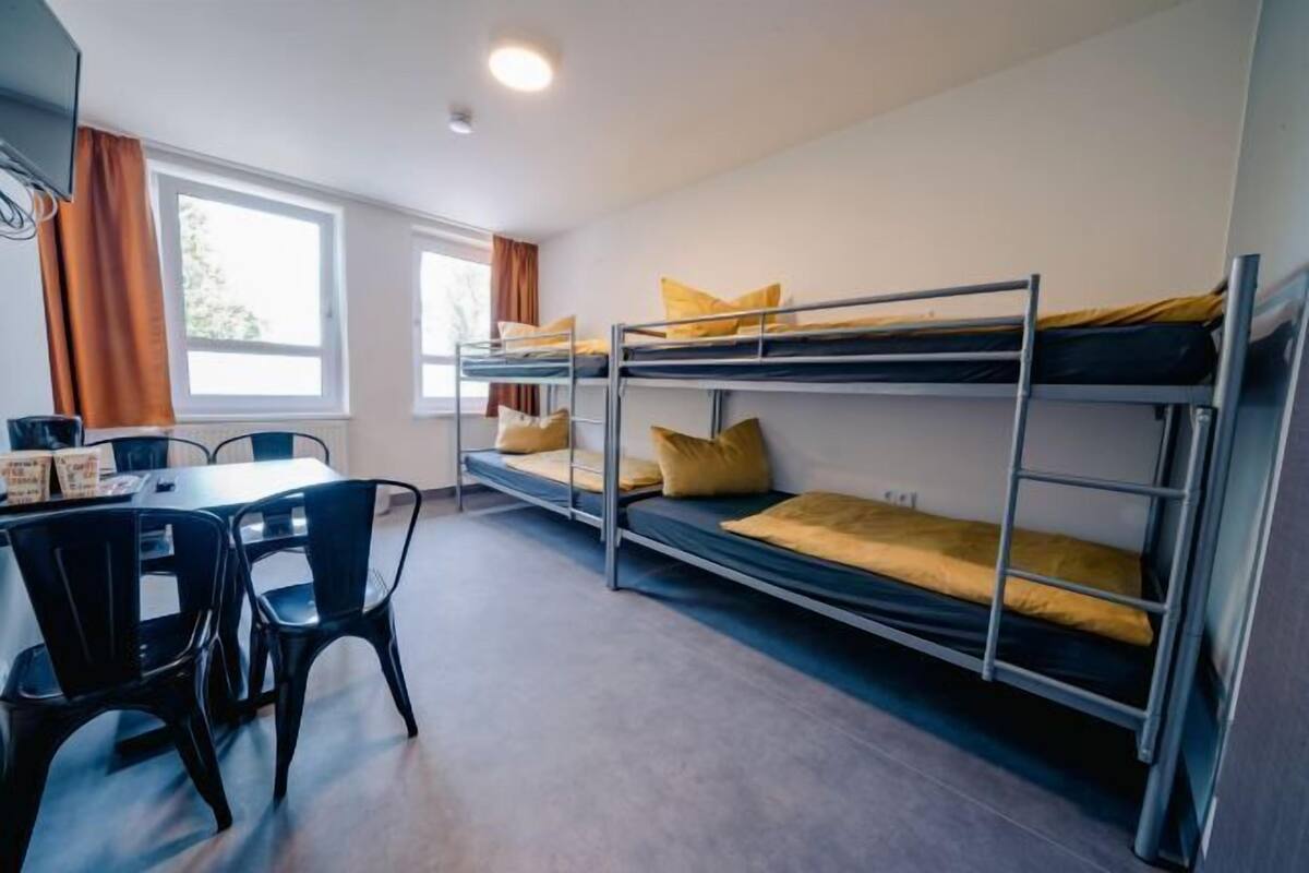 Ein Schlafsaalzimmer mit Etagenbetten, einem Tisch, Stühlen und einem Fenster.