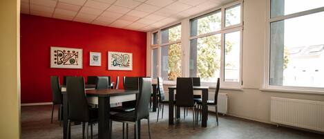 A dining area with red walls, multiple tables and chairs, and large windows with a view of trees.
