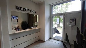 A reception area with a sign reading "RECEPTION," a counter with a computer, and a door leading outside. - NEOHOSTEL Berlin (Berlin)