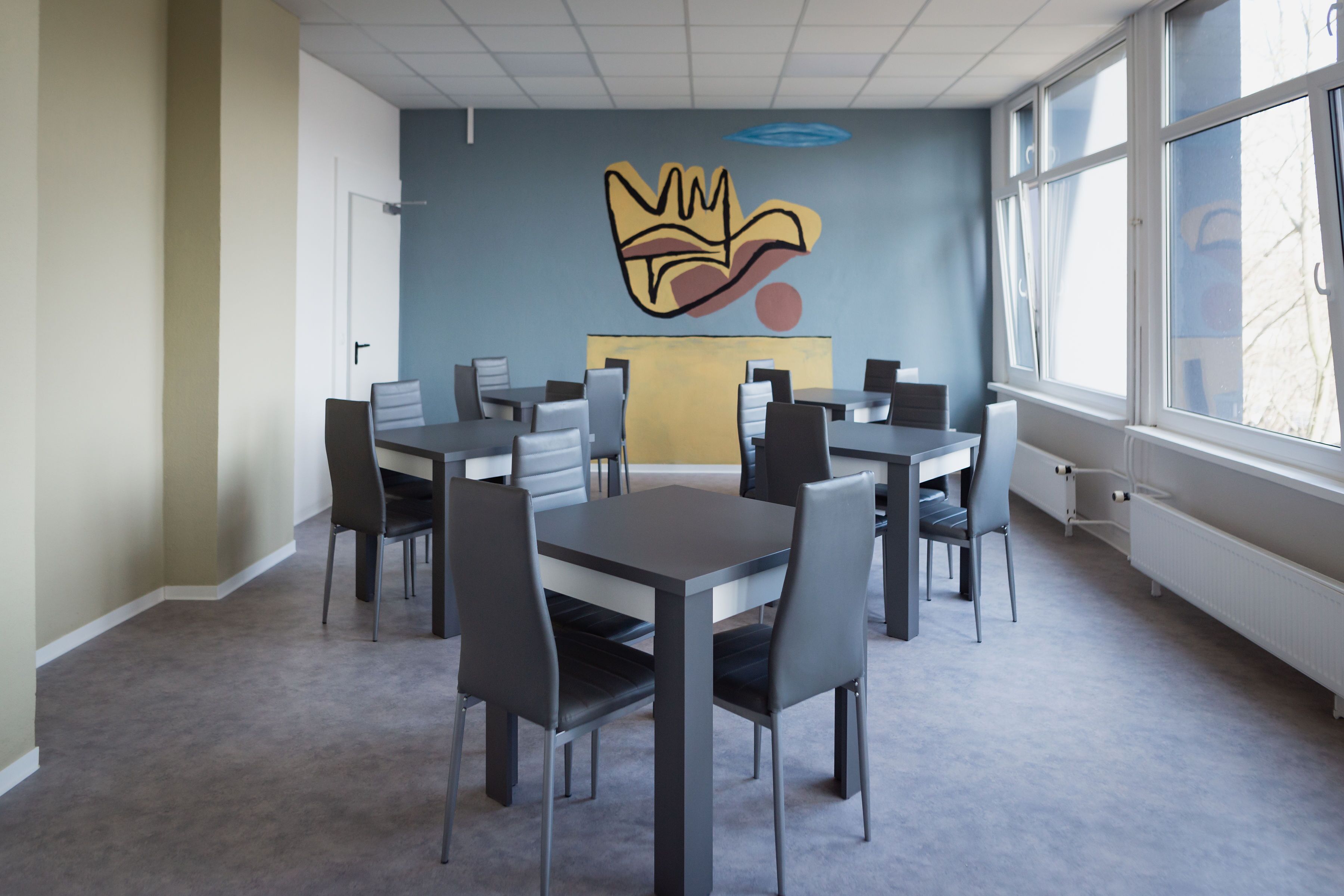 A modern dining area with tables and chairs, a large window, and a wall mural.
