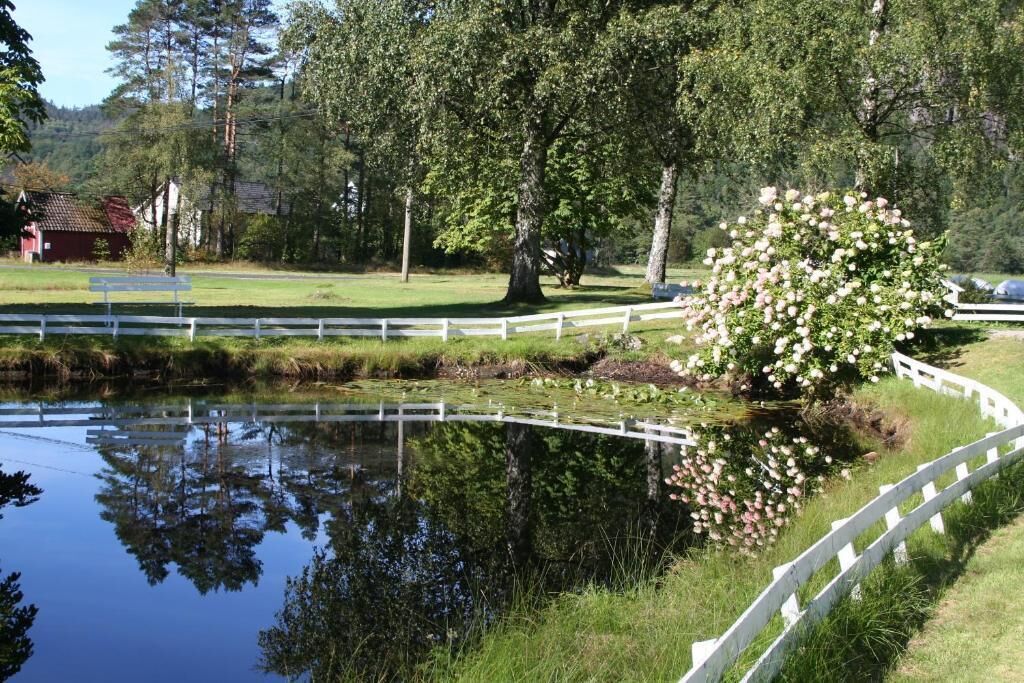 A serene pond with a white fence, lush greenery, and a blooming tree.
