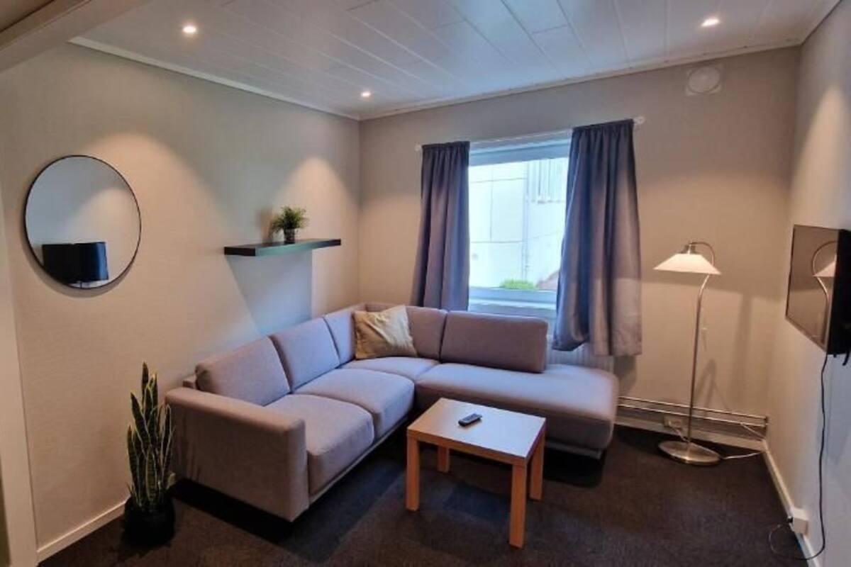 Ett modernt vardagsrum med en beige soffa, ett litet bord, en rund spegel och en golvlampa.