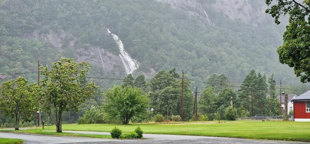 Ländliche Landschaft mit einem Wasserfall, Bäumen und einem roten Gebäude.