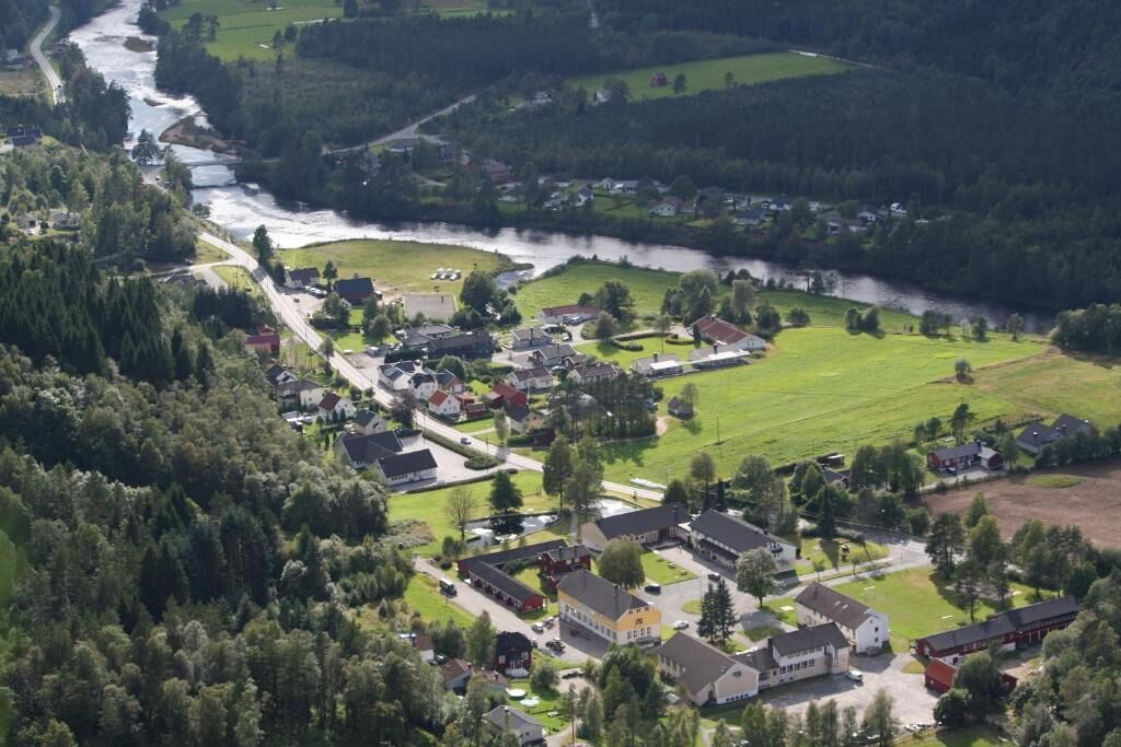An aerial view of a small town with a river running through it, surrounded by greenery and houses.
