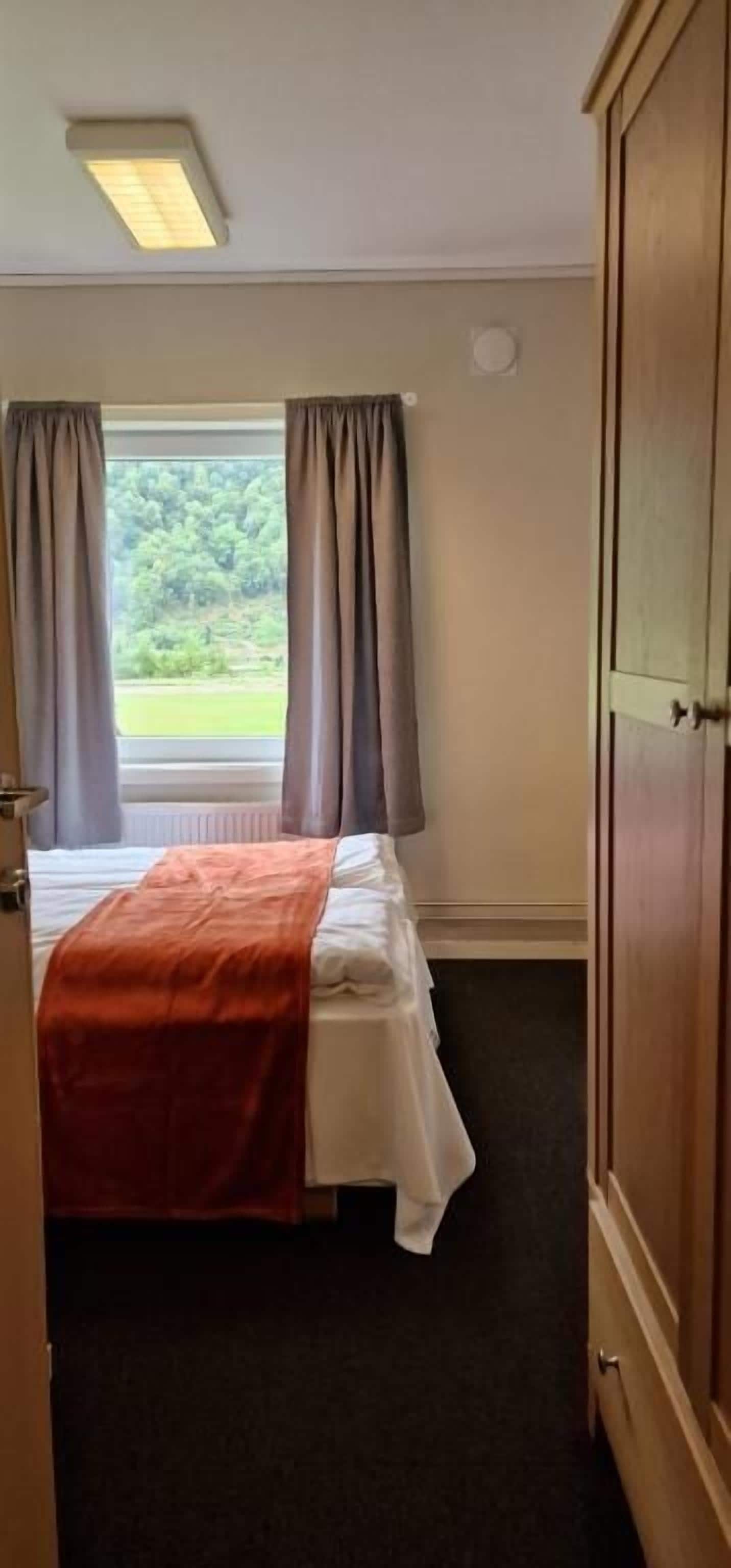 Une chambre à coucher avec un lit, une fenêtre avec des rideaux, un radiateur et une armoire.