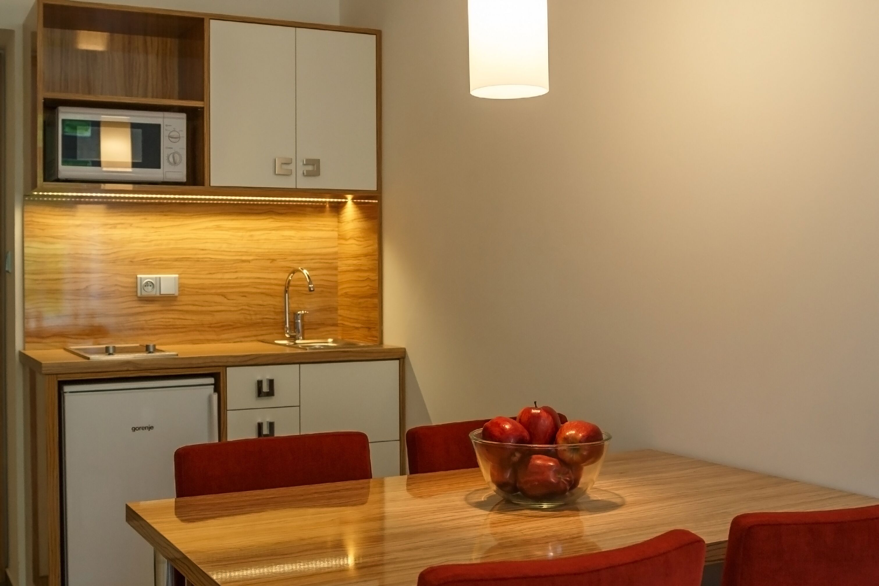 Uma cozinha compacta com micro-ondas, pia e uma área de refeições com mesa de madeira e cadeiras vermelhas.