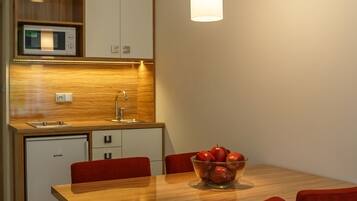 Uma cozinha compacta com micro-ondas, pia e uma área de refeições com mesa de madeira e cadeiras vermelhas.