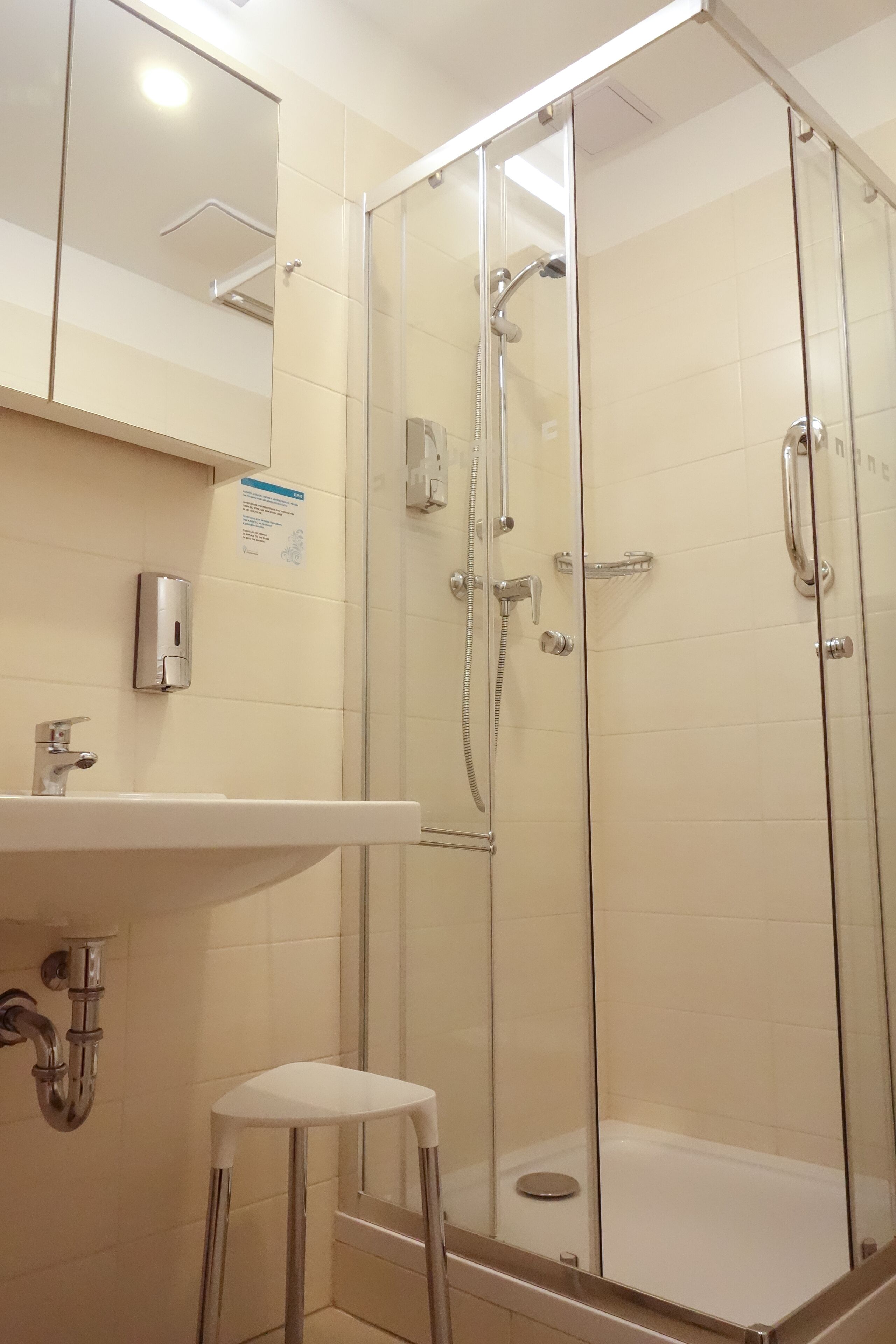 Un baño moderno con ducha envuelta en vidrio, un lavabo blanco y un taburete pequeño.