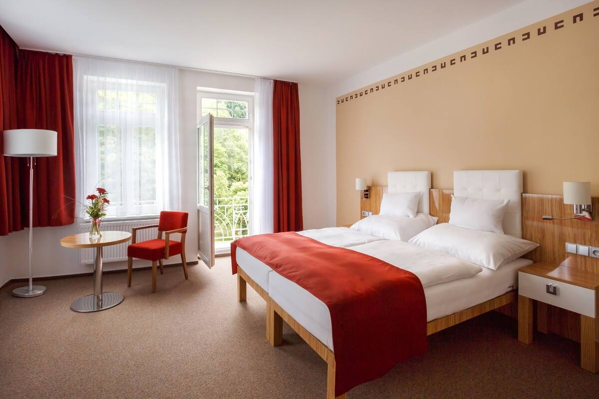 A hotel room with a bed, a chair, a table, and a window with curtains.