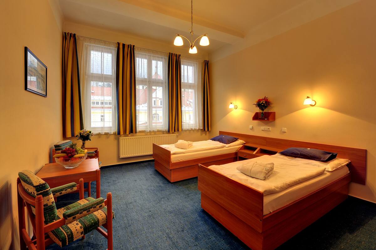 A hotel room with two beds, a wooden desk, a chair, and a window with curtains.