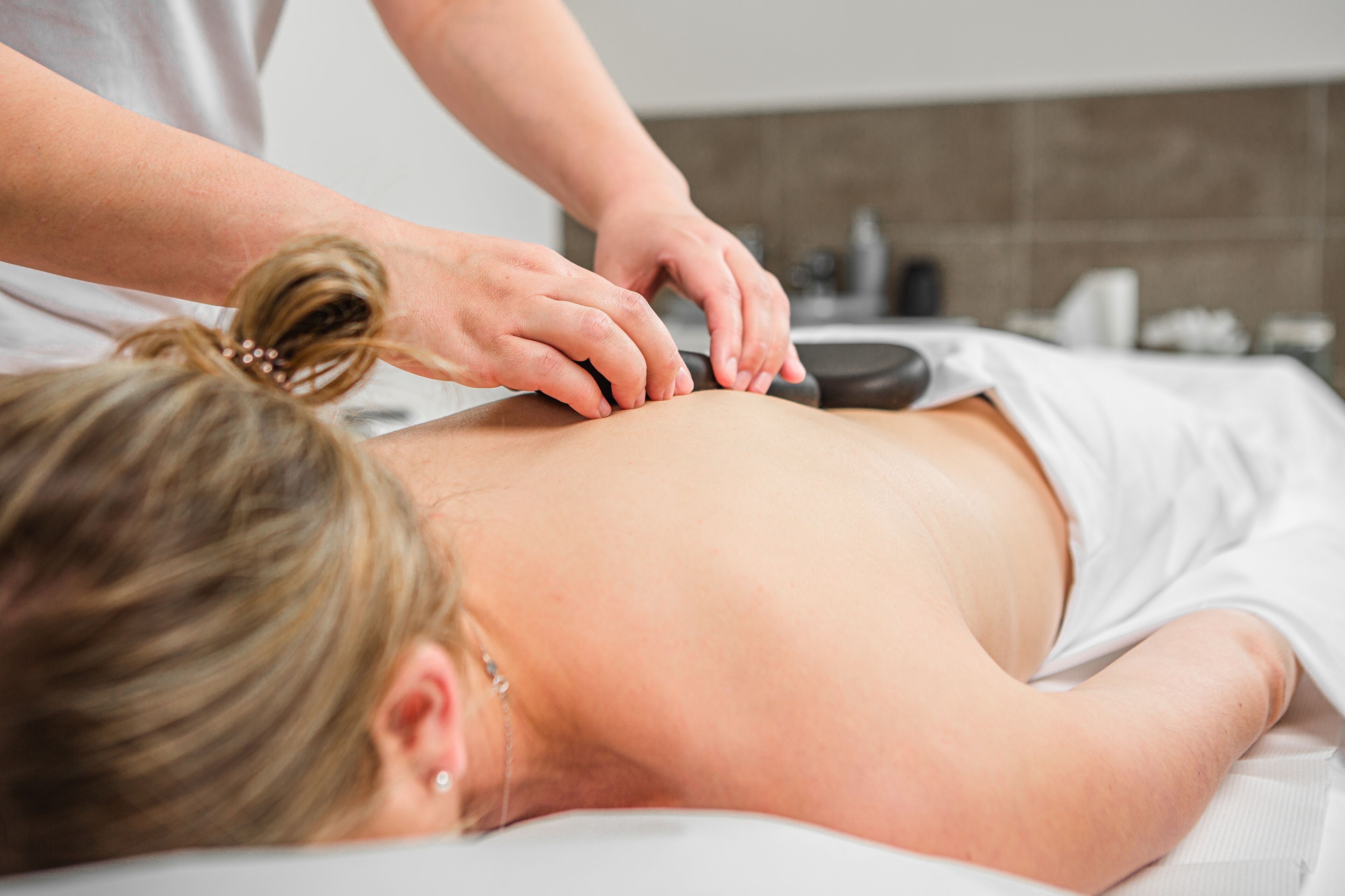 A person receiving a massage on a massage table in a room with a tiled wall and a white ceiling.
