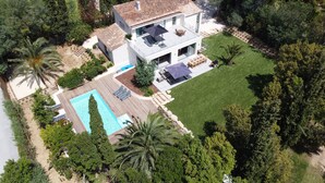 Une maison moderne à deux étages avec une piscine, entourée d’une végétation luxuriante et d’arbres.