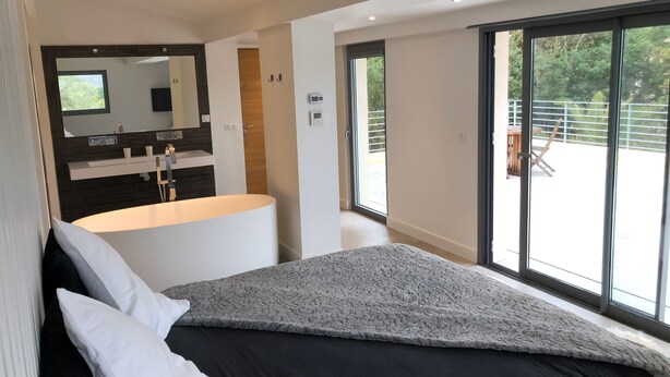 Une chambre moderne dotée d’un grand lit, d’une coiffeuse intégrée avec un miroir et d’une porte-fenêtre coulissante donnant sur un espace extérieur.