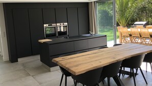 Une cuisine moderne avec des meubles de rangement noirs, deux fours encastrés et une grande table à manger en bois, assortie de chaises noires.