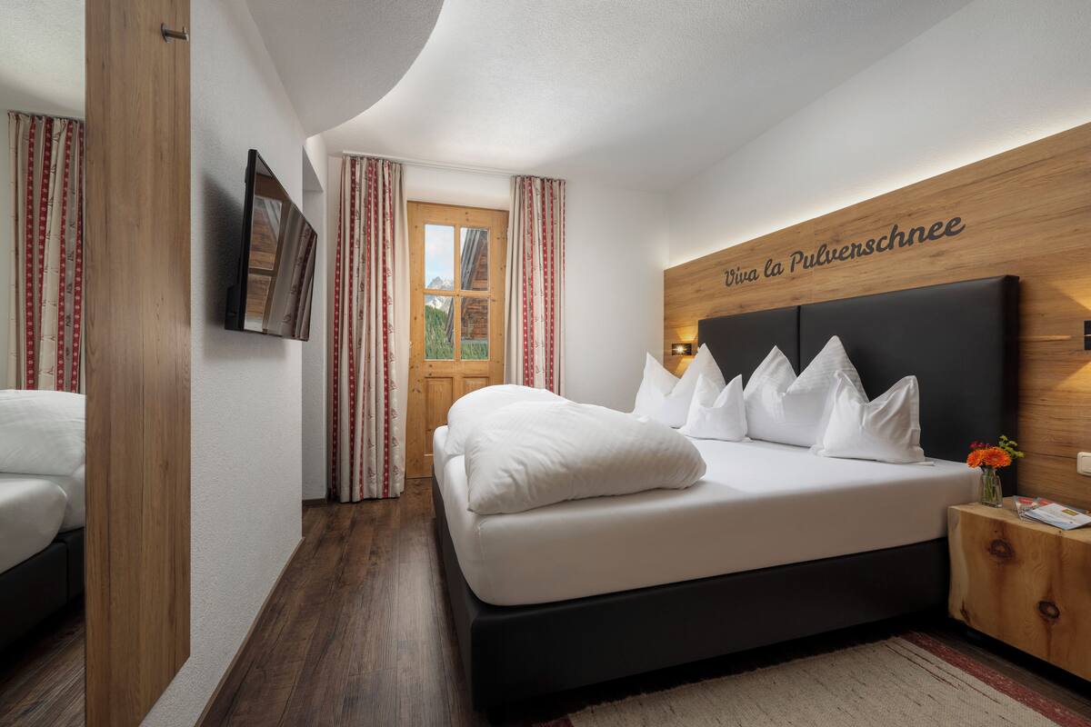 Une chambre d’hôtel moderne avec un grand lit, une tête de lit en bois et un téléviseur fixé au mur.