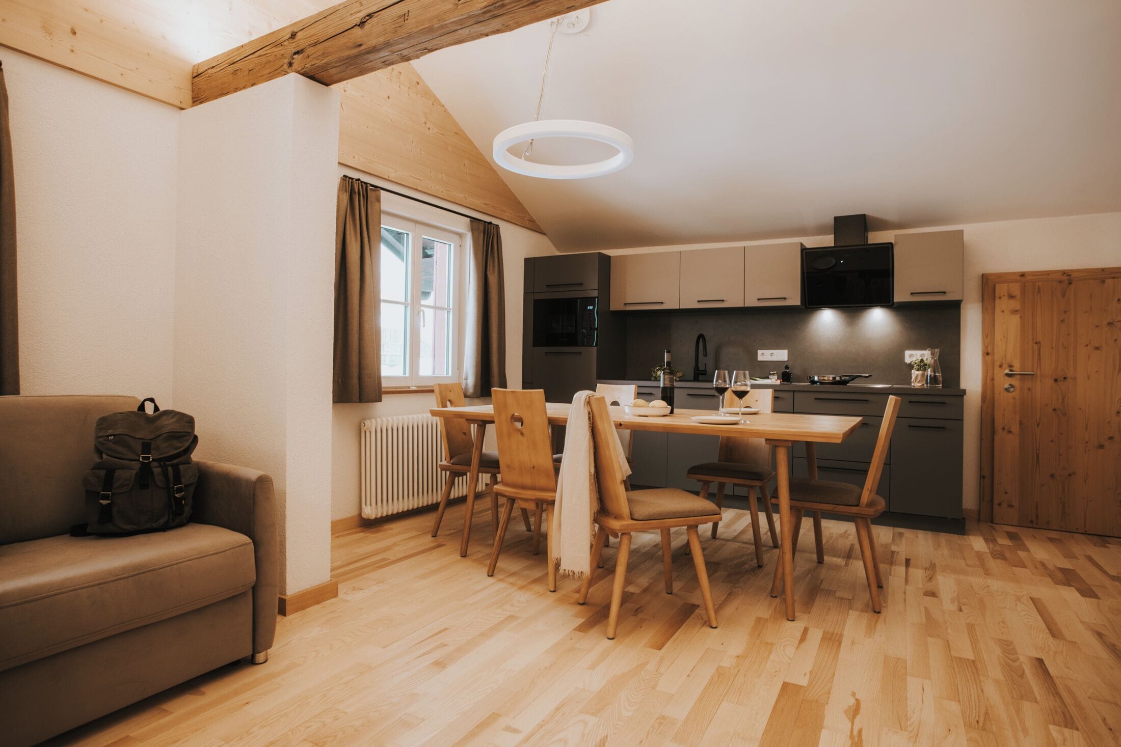 A cozy kitchen with wooden cabinets, a dining table with chairs, a sofa, and a radiator.