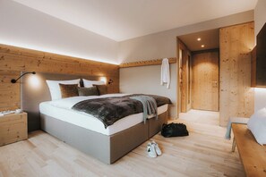 A modern bedroom with a wooden headboard, a large bed with pillows, a bedside table, and a bench. - Landhaus Albert Murr (Sankt Anton am Arlberg)