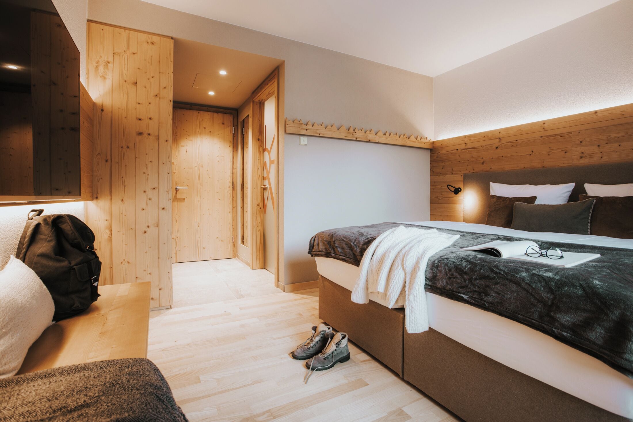 A bedroom with a bed, a bedside table, a wooden wardrobe, and a door leading to another room.