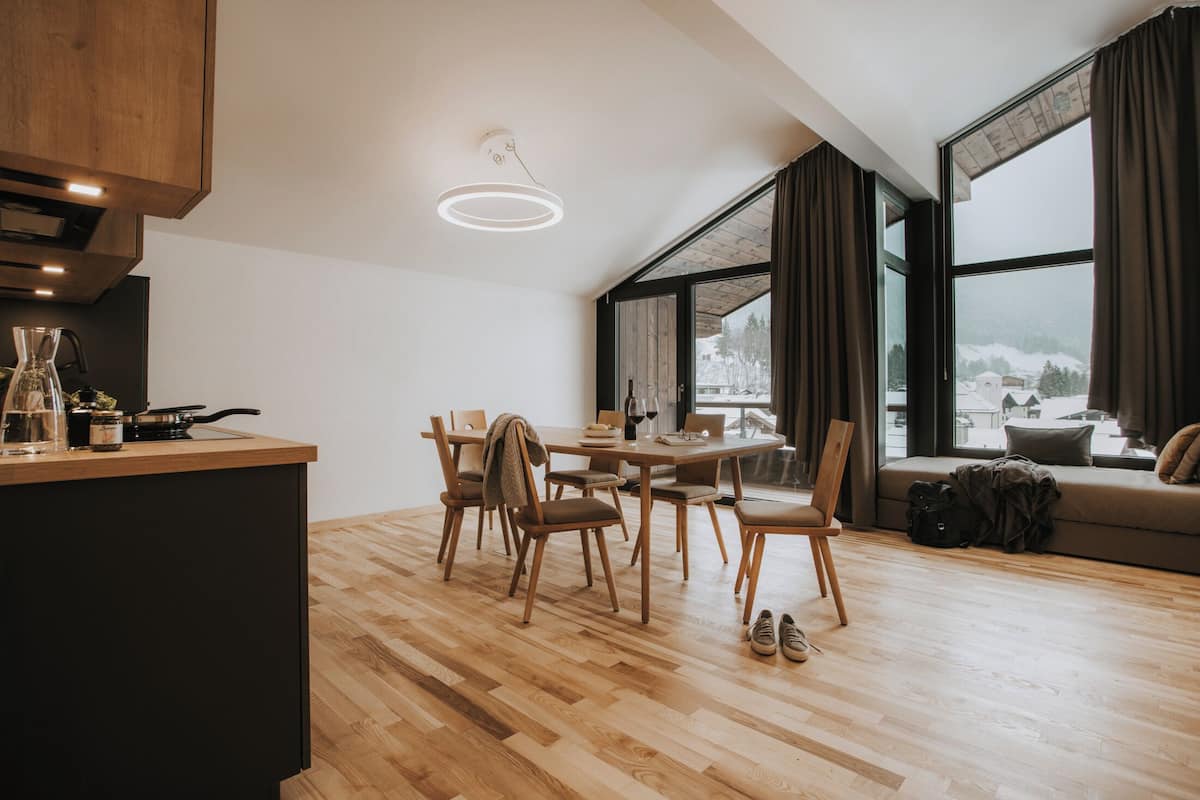 Une cuisine moderne avec des meubles en bois, un coin repas comprenant une table et des chaises, et de grandes fenêtres offrant une vue sur un paysage enneigé.