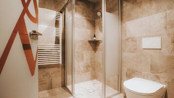 Ein modernes Badezimmer mit Duschkabine aus Glas, einer weißen Toilette und beige gefliesten Wänden.