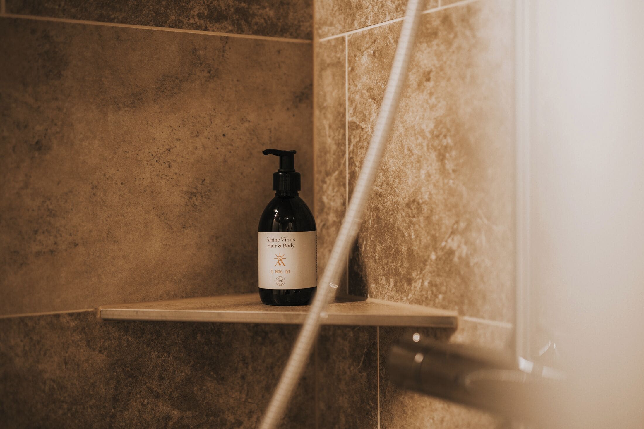 A bottle of Alpine Vibes Hair & Body on a shelf in a bathroom with beige tiles.
