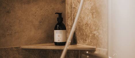 A bottle of Alpine Vibes Hair & Body on a shelf in a bathroom with beige tiles.