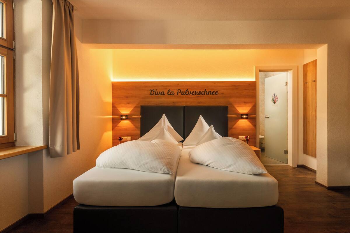 Une chambre d’hôtel avec un lit double, deux tables de chevet, une tête de lit en bois et un luminaire fixé au mur.