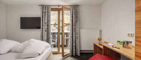 Habitación de hotel con cama, escritorio, una otomana roja, televisor y vista a un edificio a través de una puerta de cristal.