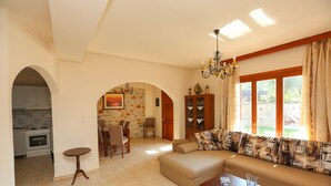 Una sala de estar con un sofá, una mesa de centro y un comedor con sillas y una mesa. Se ve una cocina a través de un arco.