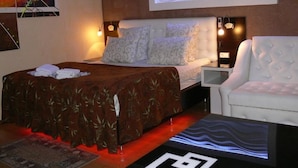 A modern hotel room with a large bed, a white armchair, and a desk with a lamp. - Apart Hotel Dom (Odesa)