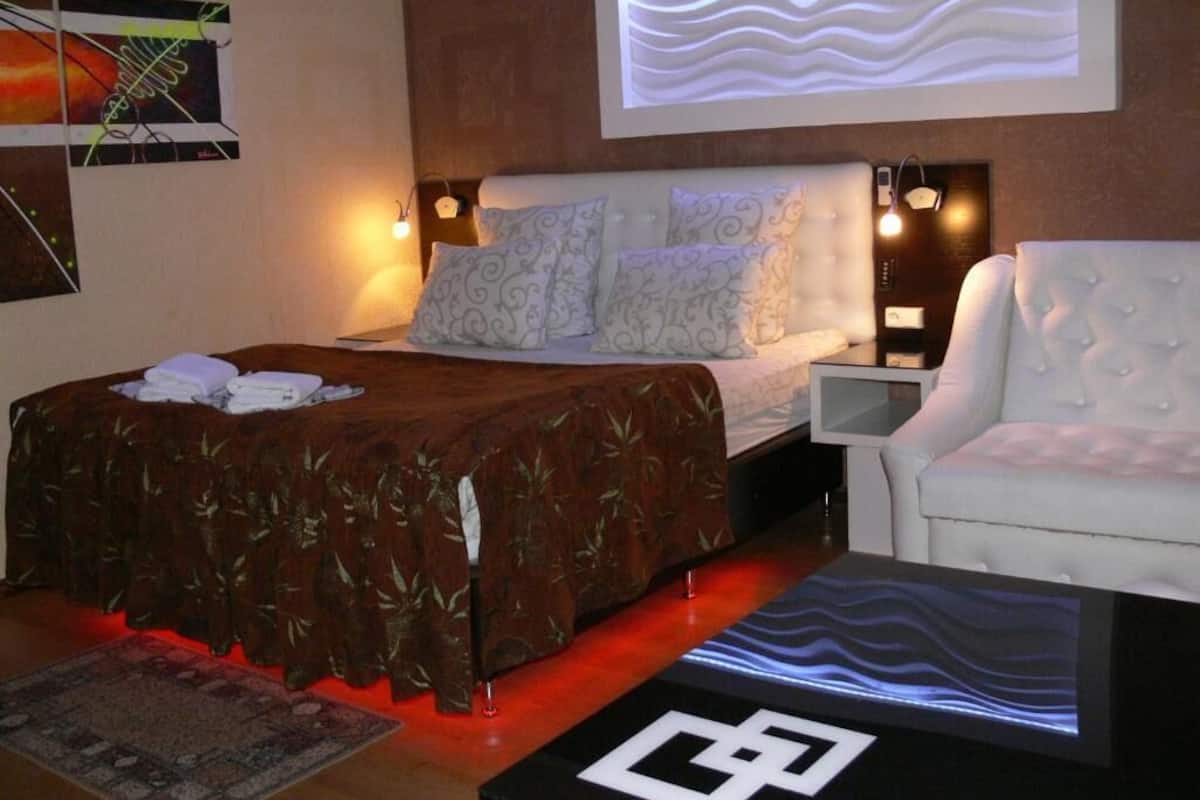 A modern hotel room with a large bed, a white armchair, and a desk with a lamp.